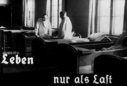 This photo originates from a film produced by the Reich Propaganda Ministry. It shows two doctors in a ward in an unidentified asylum. The existence of the patients in the ward is described as "life only as a burden." Such propaganda images were intended to develop public sympathy for the Euthanasia Program.