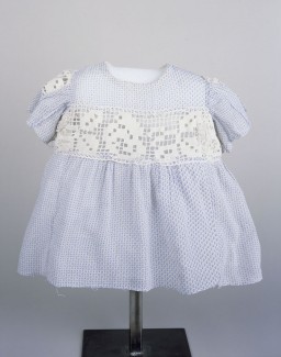 A blue and white child's dress worn by Sabina Kagan while living in hiding with the Roztropowicz family in Radziwillow, Poland, during World War II. Her rescuers used doll's clothing to make this dress.
Sabina was just an infant when SS mobile killing squads began rounding up Jews in the Polish village of Radziwillow in 1942. Her parents persuaded a local policeman to hide the family. The policeman, however, soon asked the Kagans to leave but agreed to hide baby Sabina. Her parents were captured and killed. Sabina was concealed in a dark basement, with minimal food and clothing. She was discovered and taken in by the Roztropowicz family in 1943. Like most hidden children, Sabina had few personal belongings. Her foster mother Natalia even made her some clothing from doll clothes. This blue and white dress with crochet inserts in the waist and sleeves is one of the few pieces of clothing Sabina had. It measures just 13 inches from neck to hemline.