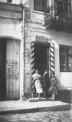Malcia, Matla ve Rachel Saleschutz, annelerinin dükkânının önünde simit yiyor. Kapı çerçevesindeki kırmızı ve beyaz çizgiler, dükkânda sigara, kibrit, şeker ve devlet tekelince düzenlenen tüketim maddeleri bulunduğunu gösteriyor. Kolbuszowa, Polonya, 1934.