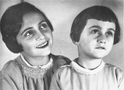 Black and white portrait of two young girls with light skin tone and dark short hair. The girl on the left has a big smile, while the girl on the right has a much more reserved smile. Both are looking towards the top right.