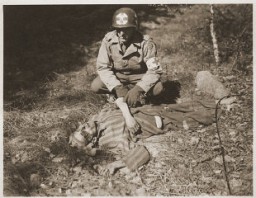 An American soldier kneels by the corpse of a prisoner on the roadside near Gardelegen. The prisoner was shot by the SS when he was too exhausted to continue on a death march. Germany, April 14-18, 1945.