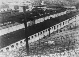 View, through the barbed wire, of the prisoner barracks in the Flossenbürg concentration camp. [LCID: 06012]
