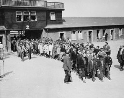 Escorted by US soldiers, child survivors of the Buchenwald concentration camp file out of the main gate of the camp. Buchenwald, Germany, April 27, 1945.