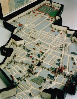 Leon Jakubowicz, a shoemaker by training and a native of Lodz, began constructing this model of the Lodz ghetto soon after his arrival there from a prisoner-of-war camp in April 1940. The case holds a scale (1:5000) model of the ghetto, including streets, painted houses, bridges, churches, synagogue ruins, factories, cemeteries, and barbed wire around the ghetto edges. The model pieces are made from scrap wood. The case cover interior is lined with a collection of official seals, a ration card, and paper money, and the case exterior is covered with metal coins.