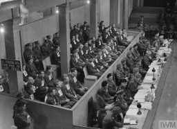 Wearing numbers, the defendants in the Bergen-Belsen Trial sit in the courtroom in Lüneburg, Germany. The Belsen Trial began on September 17, 1945, and was one of the first war crimes trials held after World War II. IWM (HU 59545)