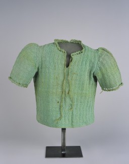 Green knit child’s sweater with short slightly puffed sleeves. There are two around the scalloped collar used to make a bow.