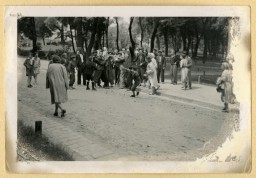 Photograph of bystanders watching as a young boy attacks a man with a broom on a street in Lwow during the pogrom of July 1, 1941.