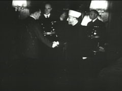 In this German propaganda newsreel, the former Mufti of Jerusalem, Hajj Amin al-Husayni, an Arab nationalist and prominent Muslim religious leader, meets Hitler for the first time. During the meeting, held in in the Reich chancellery, Hitler declined to grant al-Husayni’s request for a public statement--or a secret but formal treaty--in which Germany would: 1) pledge not to occupy Arab land, 2) recognize Arab striving for independence, and 3) support the “removal” of the proposed Jewish homeland in Palestine. The Führer confirmed that the “struggle against a Jewish homeland in Palestine” would be part of the struggle against the Jews. Hitler stated that: he would “continue the struggle until the complete destruction of Jewish-Communist European empire”; and when the German army was in proximity to the Arab world, Germany would issue “an assurance to the Arab world” that “the hour of liberation was at hand.” It would then be al-Husayni’s “responsibility to unleash the Arab action that he has secretly prepared.” The Führer stated that Germany would not intervene in internal Arab matters and that the only German “goal at that time would be the annihilation of Jewry living in Arab space under the protection of British power.”