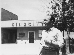 Edward Arzt, a Jewish displaced person (DP), stands at the entrance to the Cinecittà DP camp in Rome, Italy, 1947. Arzt and his family lived in the camp for three years before immigrating to the United States.