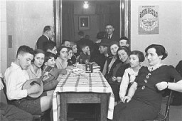 Members of the Chug Ivri (Hebrew Club) in Berlin celebrate Purim with food and song. On the wall is an advertisement for Juedische Rundschau, the newspaper of the German Zionist movement. Berlin, Germany, 1935.