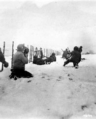 John Perry, a movie photographer with Unit 129, films GIs of the 290th Infantry Regiment, 75th Infantry Division, and 4th Cavalry Group ferreting out German snipers near Beffe, Belgium, in early January 1945. Twelve Germans were killed. The scene was photographed by Carmen Corrado of the 129th. January 7, 1945. US Army Signal Corps photograph taken by C.A. Corrado.