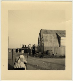 A young baby sits in its carriage next to a Quonset hut in Babenhausen displaced persons camp. [LCID: 54644]