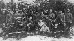 Group portrait of members of the Kalinin Jewish partisan unit (Bielski group) on guard duty at an airstrip in the Naliboki Forest. [LCID: 46677]