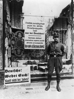 During the anti-Jewish boycott, an SA man stands outside a Jewish-owned store with a sign demanding that Germans not buy from Jews. [LCID: 4053]