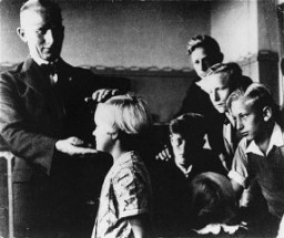 A German teacher singles out a child with "Aryan" features for special praise in class. The use of such examples taught schoolchildren to judge each other from a racial perspective. Germany, wartime.