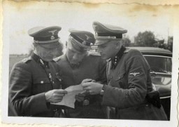 Richard Baer and Karl Höcker look over a document with SS-Standartenführer Dr. Enno Lolling, the director of the Office for Sanitation and Hygiene in the Inspectorate of Concentration Camps. From left to right: Lolling, Baer, Höcker.
From Karl Höcker's photograph album, which includes both documentation of official visits and ceremonies at Auschwitz as well as more personal photographs depicting the many social activities that he and other members of the Auschwitz camp staff enjoyed. These rare images show Nazis singing, hunting, and even trimming a Christmas tree. They provide a chilling contrast to the photographs of thousands of Hungarian Jews deported to Auschwitz at the same time. 