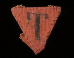 Red triangle patch worn by Czech political prisoner Karel Bruml in Theresienstadt. The letter "T" stands for "Tscheche" (Czech in German).