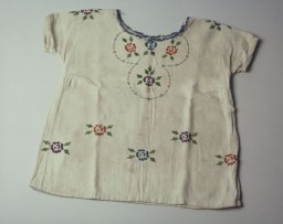 A child's dress embroidered with red and blue flowers with small green leaves. This dress was hand embroidered by Lola Kaufman's mother in the Czortkow ghetto. Lola (born Lea Rein) wore this dress when she went into hiding. Lola was hidden first under a bed in the house of the woman who used to deliver milk to the family, then in a dugout under a cellar of a barn where she joined three other Jews in hiding. In March 1944, the Soviets liberated the area. The hidden Jews left their hideout in the middle of the night. Eight-year-old Lola joined a crowd of refugees walking eastwards.