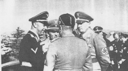 Au cours d’une visite en Allemagne, le dictateur italien Benito Mussolini (le dos à l'objectif) parle avec (de gauche à droite) : le chef SS Heinrich Himmler ; le ministre de la Propagande nazie Joseph Goebbels et le gouverneur nazi de la Pologne Hans Frank. Allemagne, 1941.