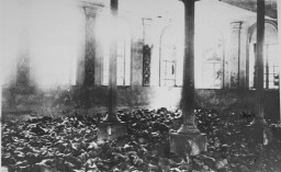 Black and white photograph of the inside of a synagogue. Piles of shoes cover the floor.