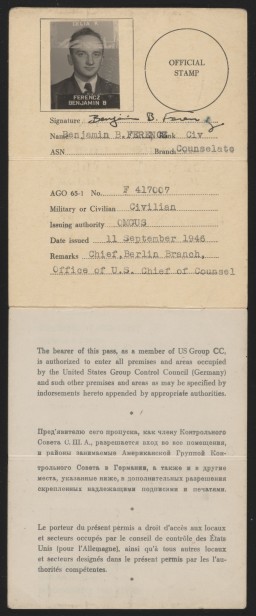 A paper pass that’s been filled out using a typewriter. At the top left is a black and white photograph of a man with light skin tone and dark hair wearing a suit. The top right has a space for an official stamp. The stamp has been embossed on the paper with part of it going over the photograph. It is signed in black ink.