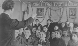 Lyrics to the Jewish national anthem and portraits of Zionist leaders hang in a classroom. [LCID: 64047]