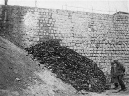 浮生堡 (Flossenbuerg) 集中营解放后，两名美军步兵检查集中营遇难者留下的鞋子。