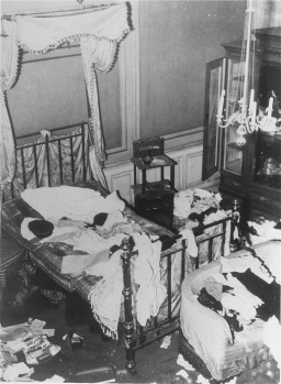 An elevated view of a home that has been vandalized. Clothes are strewn across the bed and floor. Cabinets have been opened and rummaged through. The entire room is in disarray.