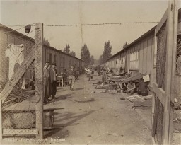 Survivors move around between rows of barracks in the newly liberated Dachau concentration camp. [LCID: 07971]