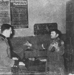 A German policeman interrogates a Jewish man accused of trying to smuggle a loaf of bread into the Warsaw ghetto. Warsaw, Poland, 1942-1943.