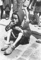 Un bambino, in condizioni di evidente denutrizione, mangia qualcosa in una strada del ghetto di Varsavia.
