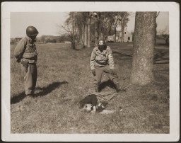 An American medic and soldier stand by the corpse of a prisoner shot on the road near Gardelegen. [LCID: 28196]