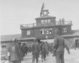 جنود أمريكان وسجناء محررون عند المدخل الرئيسي من محتشد بوخنوالد. ألمانيا, مايو 1945.