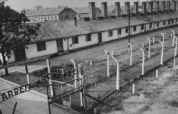 View of the kitchen barracks, the electrified fence, and the gate at the main camp of Auschwitz (Auschwitz I). In the foreground is the sign "Arbeit Macht Frei." This photograph was taken after the liberation of the camp by Soviet forces. Auschwitz, Poland, 1945.