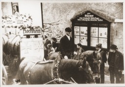 A Hochheim parade float proceeds down the Kirchstrasse, passing by a display box for Der Stürmer, an antisemitic newspaper. The display box bears the slogan, "Without a solution to the Jewish question, there is no salvation for the German people." Hochheim am Main, Germany, circa 1934–1940.