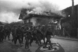 Soviet troops trample a Nazi flag as they march past a burning house on a street in the outskirts of Vienna. Photograph taken by Soviet photographer Yevgeny Khaldei. Vienna, Austria, April 1945. 