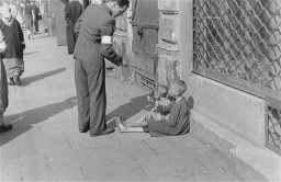 A Warsaw ghetto resident gives money to two children on a Warsaw ghetto street. [LCID: 89467]
