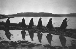 A unit of Soviet soldiers walks along a narrow strip of land that juts into the water while on a reconnaissance mission in Murmansk. Photograph taken by Soviet photographer Yevgeny Khaldei. Murmansk, Soviet Union, 1941. 
