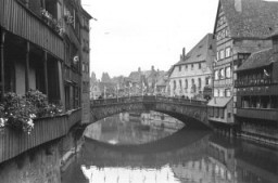 View of a bridge spanning a canal in Nuremberg. The houses and bridge are decorated with Nazi flags and banners. Photograph taken by Julien Bryan in Nuremberg, Germany, 1937.