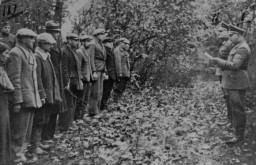 
An SD officer reads a list of charges against a group of Polish civilians just before their execution in the forest near Szubin. A German soldier can be seen in the left background and a woman is included in the number of those to be shot. According to the Main Crimes Commission, one of the officers involved is SS Major Ernst Tiedemann. Szubin (Bydgoszcz), Poland, October 21, 1939. 

