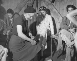 解放之后不久，一位英国妇女帮助集中营中的一名幸存者试鞋。