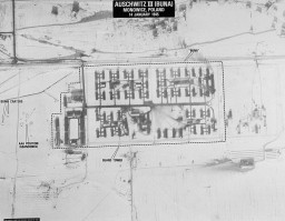 Aerial photograph of Auschwitz 3 camp. The photograph features labels of the camp boundary, the guard tower, bomb craters, and abandoned positions. There is a black label with white text at the top that reads, “Auschwitz 3 (Buna). Monowice, Poland. 14 January 1945.”