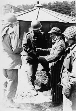 Three uniformed soldiers stand around a survivor wearing a striped uniform, a scarf, and a hat.
