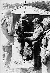 A survivor of Kaufering IV, one of the Dachau subcamps in the Landsberg-Kaufering area, with US soldiers after liberation. Kaufering, Germany, after April 27, 1945.