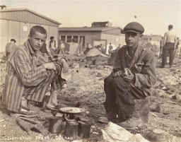 Two survivors prepare food outside the barracks. [LCID: 74095]