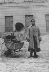 Juif tentant de gagner sa vie en jouant de la musique sur un phonographe, qu’il traîne dans une poussette. Ghetto de Varsovie, Pologne, pendant la guerre.