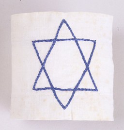 Braçadeira branca com uma Estrela de David bordada em azul, usada por Dina Offman de 1939 até 1941, enquanto estava no gueto de Stopnica, na Polônia.