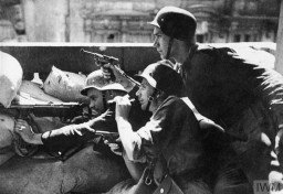 Soldiers of the Polish Home Army (Armia Krajowa) take cover behind a barricade during the Warsaw Polish uprising. During the uprising, the Home Army was supported by 2,500 soldiers from other resistance movements, such as the National Armed Forces (Narodowe Siły Zbrojne, NSZ) and the communist People's Army (Armia Ludowa, AL). Only a quarter of the partisans had access to weapons, fighting against 25,000 German soldiers equipped with artillery, tanks, and air forces. Two of the three soldiers shown here have only small handguns. August 1944.  