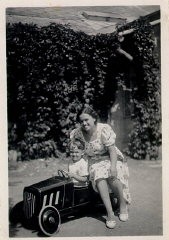 Photograph of a young Thomas Buergenthal posing in his toy car as his mother sits alongside. 1936.