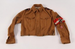 Hitler Youth summer uniform jacket with an armband and insignia designating the regiment and district to which the member belonged.  
Beginning in 1933, the Hitler Youth and its organization for girls and young women, the League of German Girls, played an important role the new Nazi regime. Through these organizations, the Nazi regime indoctrinated young people with Nazi ideology, including antisemitism and racism. All prospective members of the Hitler Youth had to be "Aryans" and "genetically healthy." Their duty was to serve Adolf Hitler and the Third Reich. Hitler Youth boys and girls were required to wear military-style uniforms, in keeping with the "soldierly" character of the Nazi Party, and conform to certain standards of behavior. Uniforms such as this one emphasized the regimented nature of the Hitler Youth. 
US Army soldier Arthur R. Myers obtained this uniform during his military service in World War II.  